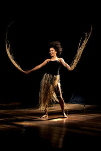 Contemporary dancer dancing in theater with black background and straw accessory. 