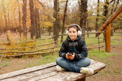 Portrait of boy sitting on wood in forest