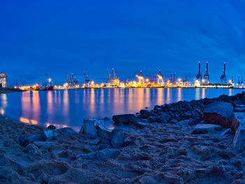 Illuminated factory by sea against sky at night