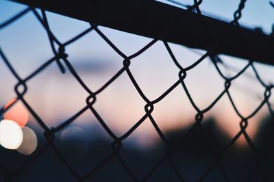 Close-up of chainlink fence against sky during sunset