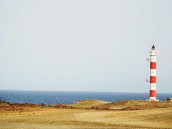 Lighthouse on beach against clear sky