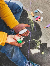 Toddler in jeans draws with crayons on the asphalt . kid's hands are covered with colorful stains. 