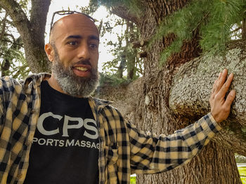 Portrait of smiling young man against tree trunk