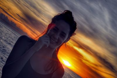 Portrait of smiling young woman with sea in background against orange sky