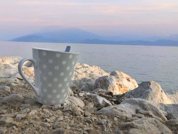 Coffee cup on rock by sea against sky