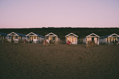 Stilt houses on beach against clear sky during sunset