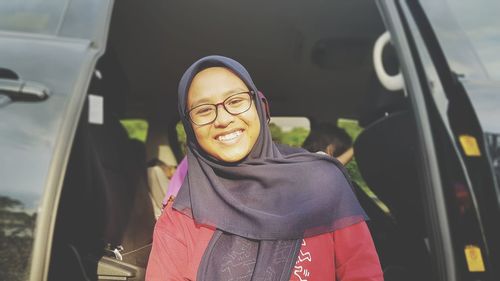 Portrait of smiling teenage girl in headscarf standing against car
