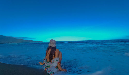 Rear view of woman standing at beach against blue sky