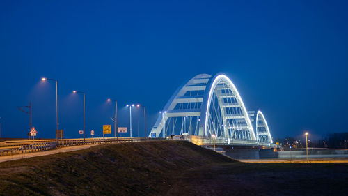 Illuminated bridge against blue sky at night