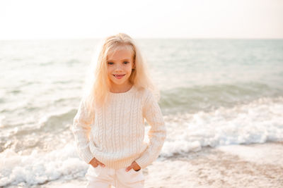 Happy smiling child girl 7-8 year old wear white knitted sweater and pants posing over nature sea