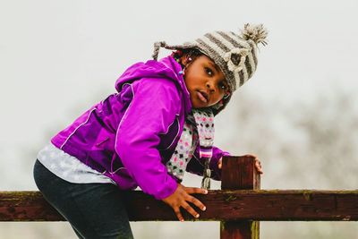 Close-up of girl wearing warm clothing sitting on wooden railing
