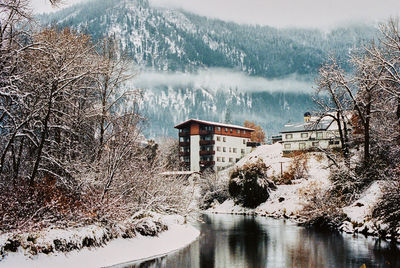 Frozen lake by trees and buildings during winter