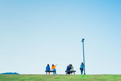 People sit and relax on field against clear sky