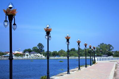 Street lights by sea against clear blue sky