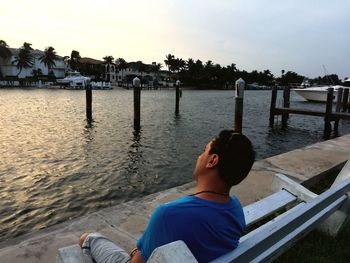 Man sitting at beach against sky during sunset