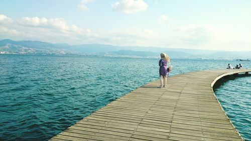 Woman standing on pier over sea against sky