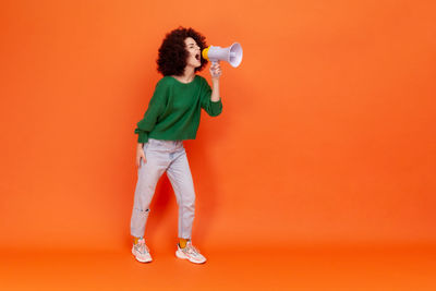 Full length of young woman standing against yellow background