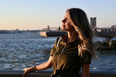 Side view of young woman looking at sea against sky during sunset