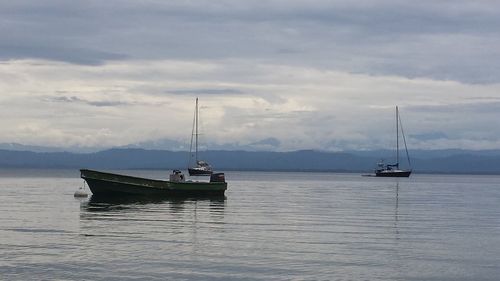 Boats sailing in calm sea against cloudy sky