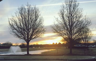 Bare trees by lake against sky during sunset