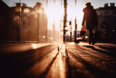 Surface level view of woman walking on sidewalk in city during sunset