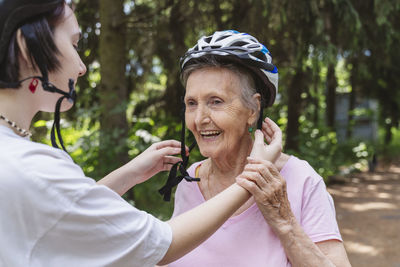 Great granddaughter helping senior woman wearing bicycle helmet in park