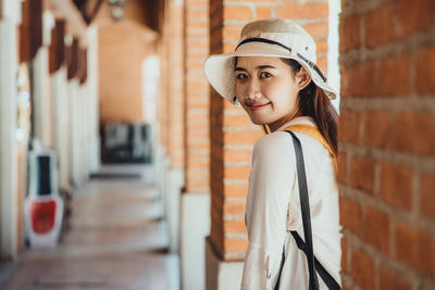 Portrait of smiling young woman standing against brick wall