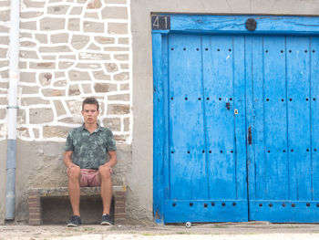 Portrait of young man sitting on seat by old building