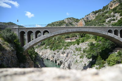 Arch bridge over river amidst trees against sky