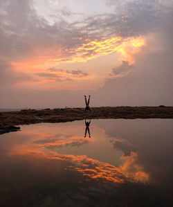 Man doing handstand reflecting on lake during sunset