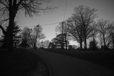 Silhouette bare trees by road against sky