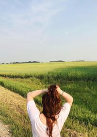 Woman tying hair on field against sky