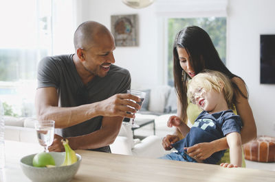 Smiling parents sitting with son while having drink at table