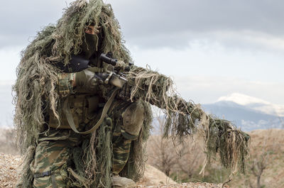 Army man in ghillie suit with rifle on field