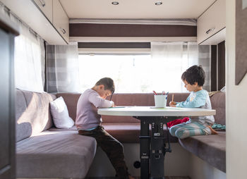Two caucasian boy paints inside caravan on weekend trip.