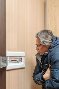 An adult man in a warm jacket looks at the electrical panel. energy saving concept. expensive 