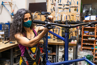 Side view of female worker in protective mask installing break and transmission wires on bicycle during maintenance service in workshop