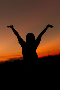 Silhouette man with arms raised against sky during sunset