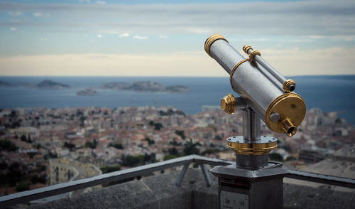 Close-up of coin-operated binoculars by cityscape against sky