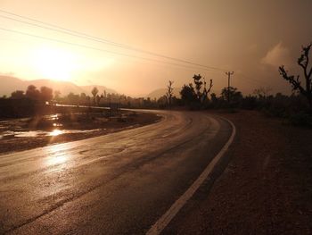 Road by trees against sky during sunset