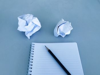 High angle view of crumpled paper balls and book with pencil on blue background