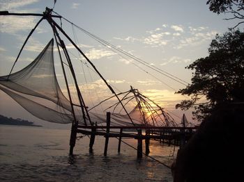 Silhouette of fishing net in sea against sunset sky