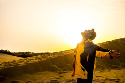 Man standing on sand at beach against sky during sunset