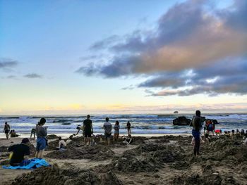 People on beach against sky during sunset