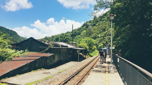 Rear view of man and woman walking on railroad station platform by houses