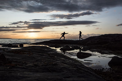 Silhouette people on beach against sky during sunset