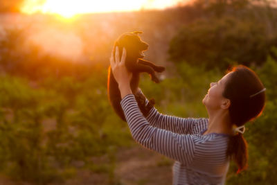 Side view of young woman holding puppy on field