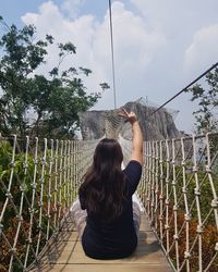 Rear view of woman sitting by plants against sky