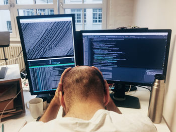 Rear view of frustrated computer programmer in front of computers in office