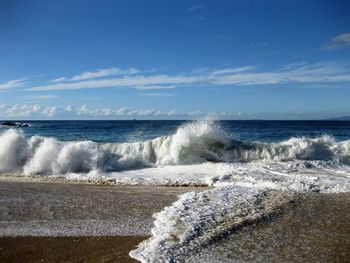 Waves splashing on shore against blue sky